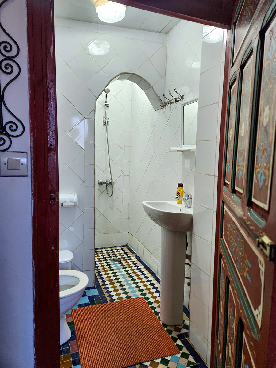 Clean private bathroom for the twin room in Riad Fez with white wall tiles, traditional Moroccan zellije floor, and an arched shower.