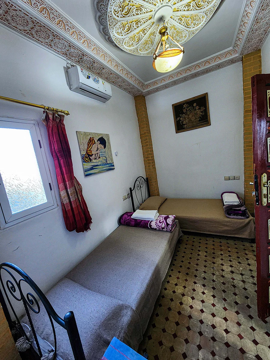 Authentic Twin Room in a Fez Riad featuring two comfortable single beds, a modern AC unit, and a beautifully detailed carved plaster ceiling.
