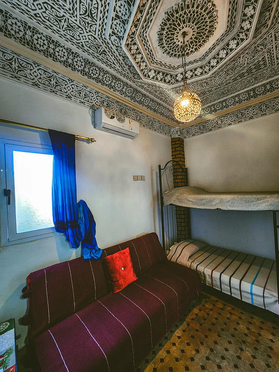 View of a budget-friendly room in a Fez Medina Riad with a window for natural light, a bunk bed, and an authentic Moroccan lantern.