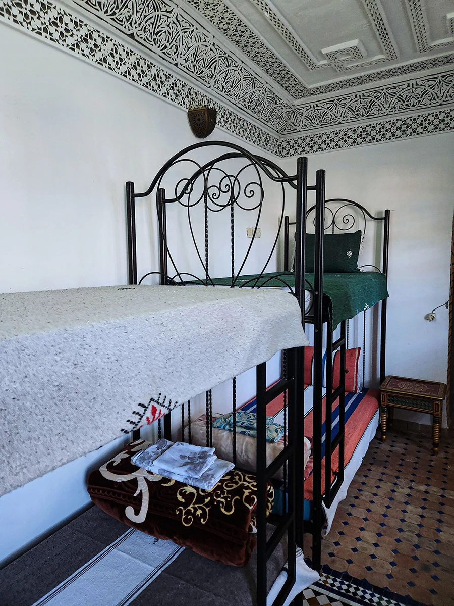 Close-up of bunk beds in a shared family room at a Moroccan Riad in Fez, showing traditional blankets and a hand-painted wooden side table.