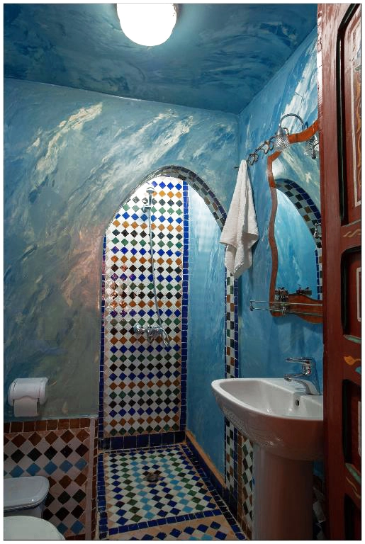 Private bathroom of the Deluxe Suite featuring an arched shower entry with colorful Moroccan Zellije tiles and blue wall finishes.