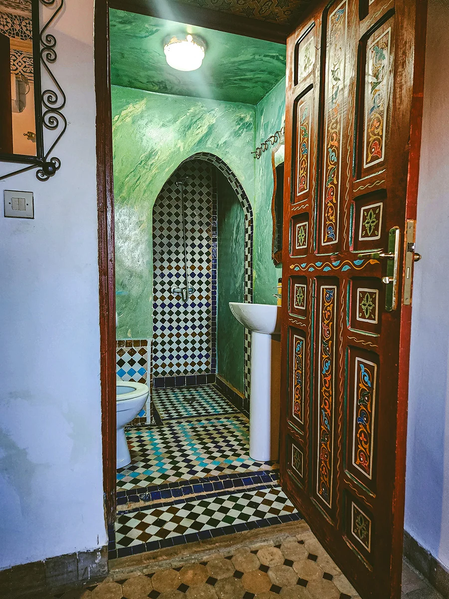 Private bathroom of the economy room in Riad Fez showcasing vibrant green Tadelakt walls and traditional colorful Zellije tile flooring.
