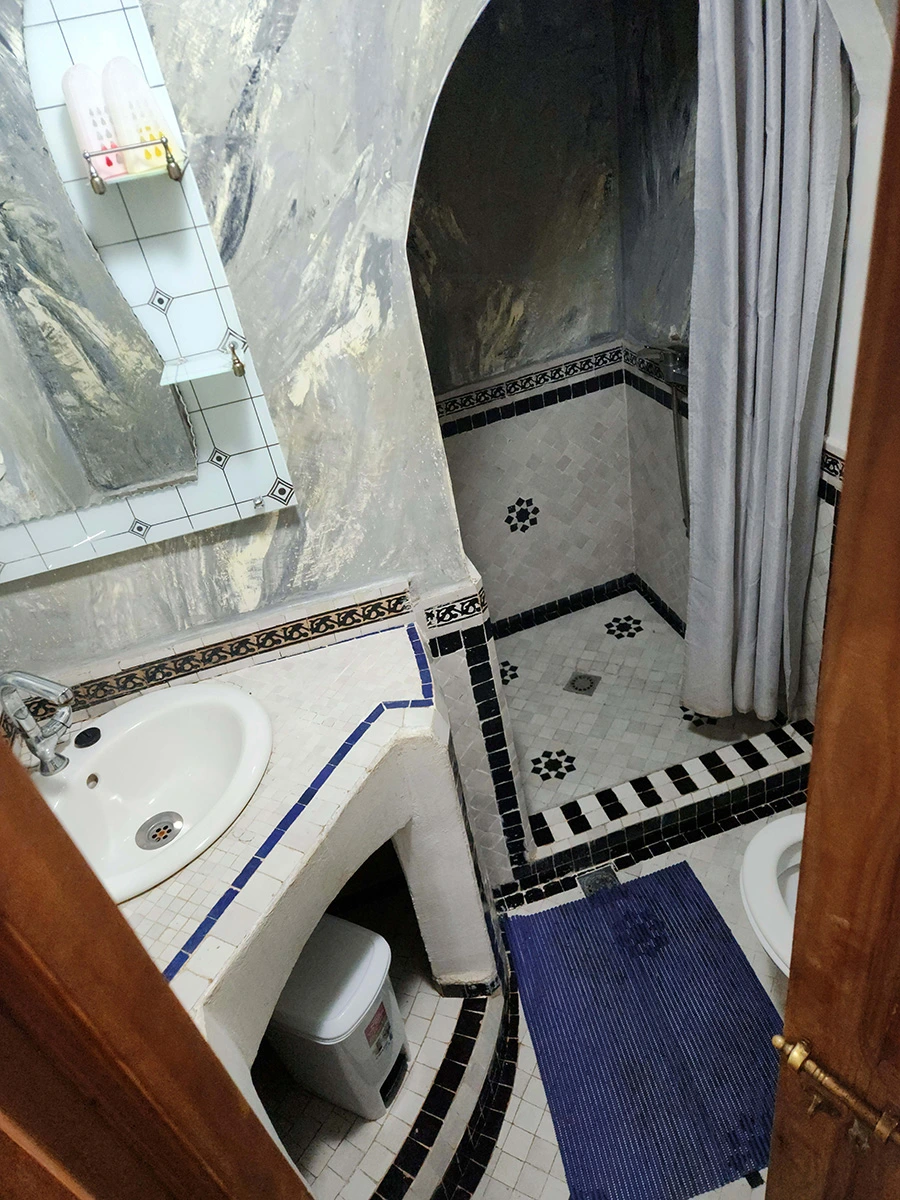 Modern private bathroom in the Grand Family Suite with traditional black and white tile borders, a white sink, and an arched walk-in shower area.