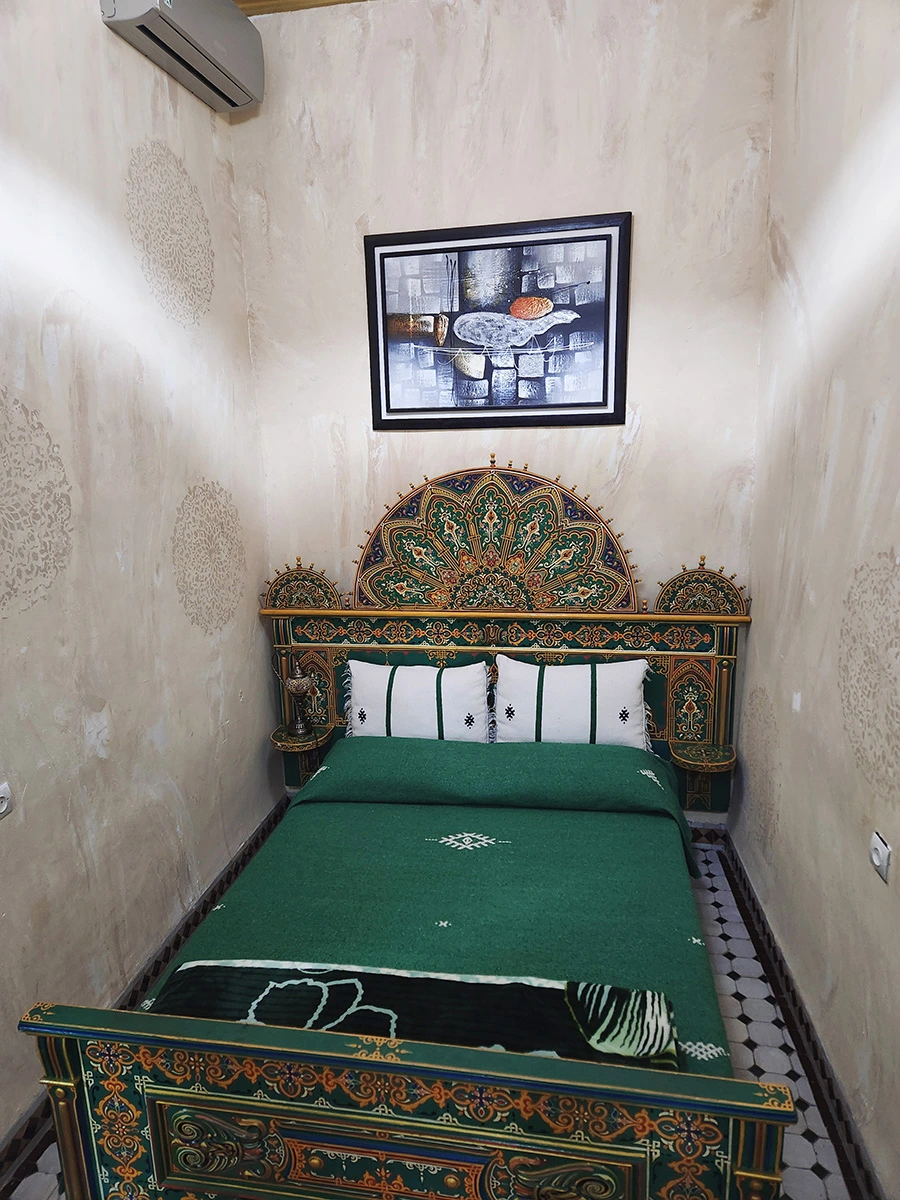 Detailed view of the luxurious green wooden headboard in the Royal Heritage Suite, showcasing intricate Moroccan craftsmanship and traditional art above the bed.