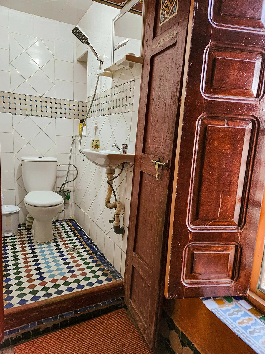 Private en-suite bathroom in a Fez Riad featuring traditional colorful Zellije tile flooring and modern shower amenities.